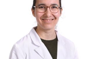 Portrait of a female medical professional wearing a white lab coat and glasses, smiling at the camera.